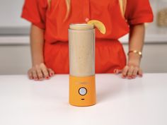 a woman sitting at a table with an orange blender on it's side