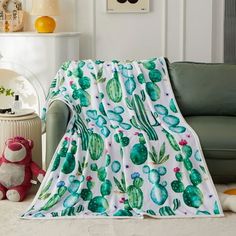 a green cactus print blanket sitting on top of a couch next to a teddy bear