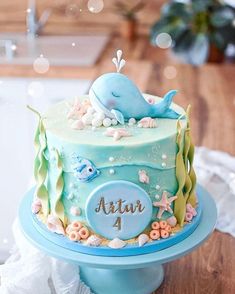 a blue and green cake with a dolphin on top sitting on a table next to other decorations