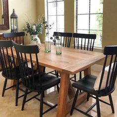 a dining room table and chairs with vases on them in front of two windows