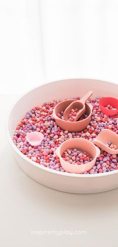 a bowl filled with lots of pink and red beads next to two spoons on top of it