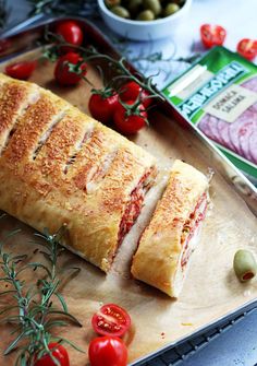 a sandwich cut in half sitting on top of a cutting board next to tomatoes and olives