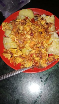 a red plate topped with food on top of a table next to a knife and fork