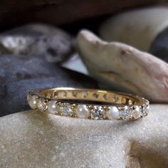 a close up of a gold ring with pearls and diamonds on top of some rocks