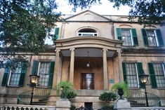 an old building with columns and green shutters on the front door is seen in this image