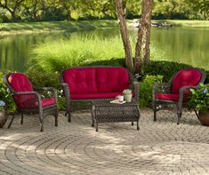 an outdoor patio with red cushions and chairs next to a pond, surrounded by greenery