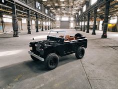 an old black jeep is parked in a large warehouse with exposed ceilings and concrete flooring