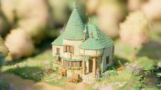 a toy house sitting on top of a lush green field next to flowers and trees