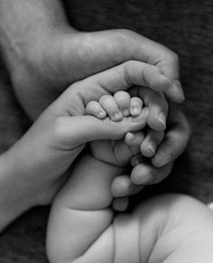 a black and white photo of two hands holding a baby's hand