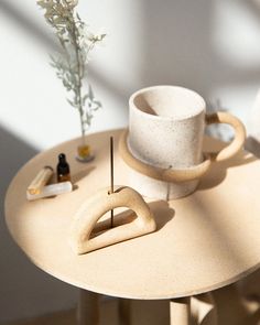 a white cup sitting on top of a wooden table next to a vase with flowers