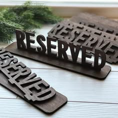 two carved wooden signs sitting on top of a white table next to a pine tree