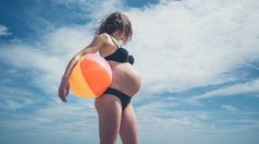 a pregnant woman on the beach with an orange and yellow ball in her belly,