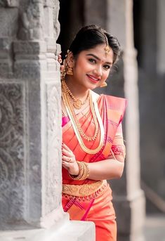 a woman in an orange and gold sari posing for the camera with her arms crossed