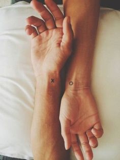 two people with matching wrist tattoos on their wrists, one is holding the other's hand