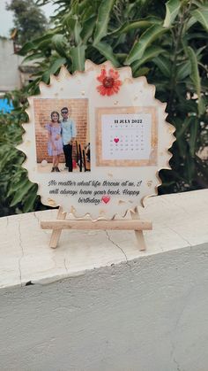 a photo frame with two photos on it sitting on a ledge in front of some trees