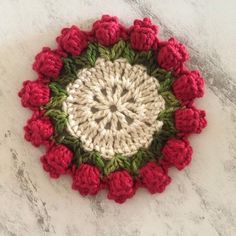 a crocheted doily with red and green flowers in the center on a marble surface