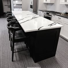 a kitchen with white cabinets and marble counter tops, black chairs and an island in the middle