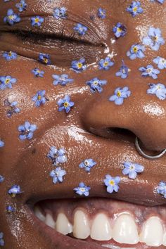 a close up of a person with flowers on her nose and nose ring in front of them