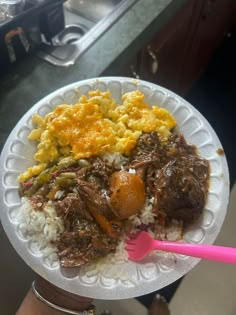 a paper plate with rice, meat and eggs on it is being held by a woman