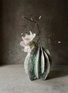 there is a vase with flowers in it on the table next to a gray wall