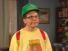 the young boy is wearing a green hat and yellow t - shirt with red suspenders