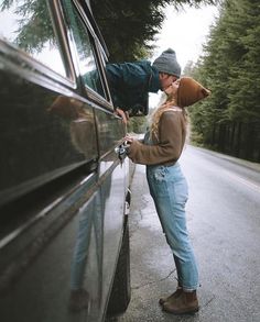 a man leaning on the side of a car while holding onto his hat and looking into the window