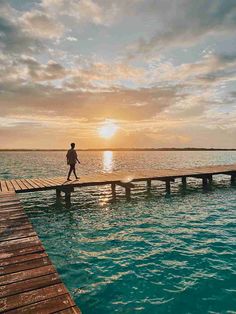 a person walking across a wooden pier over water at sunset or sunrise time with the sun setting