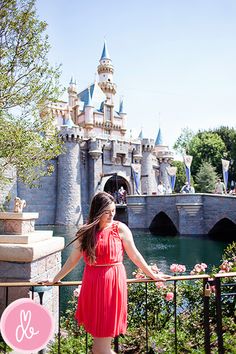 a woman in a red dress is standing on a railing near a castle and water