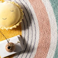 a yellow sun pillow sitting on top of a rug next to a vase with a flower in it