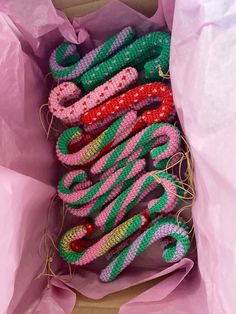 several knitted objects are in a pink bag on the floor and one is green, red, and white