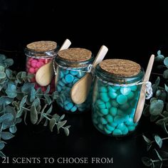 three jars filled with candy and wooden spoons on top of a table next to plants