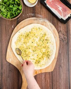 a person is making a pizza on a wooden table with other ingredients and utensils