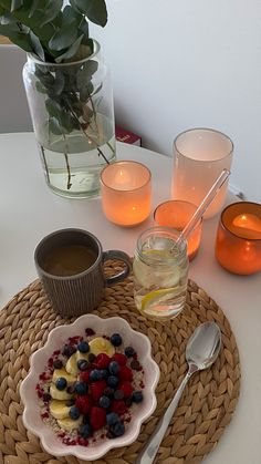 a bowl of fruit is sitting on a table next to some candles and cups with water