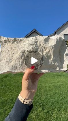 someone is holding up a rock in front of a house that has been built into the side of a hill