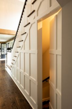 an open door leading to a living room and dining room with hardwood floors, white walls and stairs