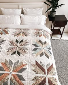 a bed with a white comforter and pillows on top of it next to a potted plant