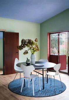 a dining room table with four chairs and a vase on top of it in front of a sliding glass door