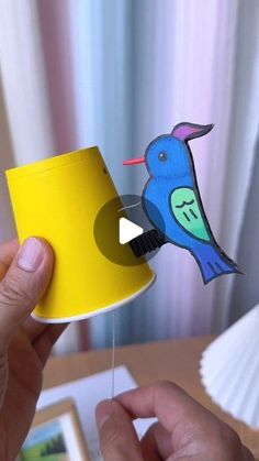 a person holding a yellow cup with a blue bird on it and a video playing in the background