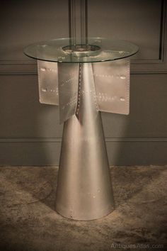 a table with a glass top and metal base on the floor in front of a wall