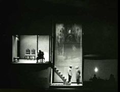 black and white photograph of two people standing in front of an open window at night