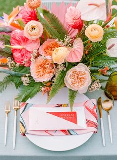 an arrangement of flowers and greenery is displayed on a white plate with silverware