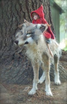 a doll is sitting on the back of a stuffed wolf in front of a tree