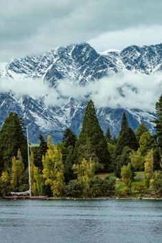 the mountains are covered in clouds and trees near a body of water with a sailboat on it