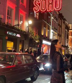 a woman walking down the street in front of a neon sign that says soho