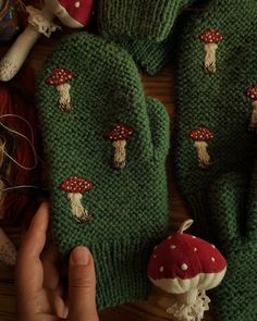 someone is holding up their green knitted mittens with mushrooms on them, which are all over the place