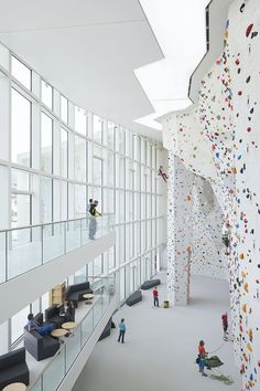 people climbing up the side of a wall in a room with high ceilings and windows