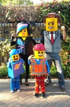 three people in lego costumes standing next to each other on a brick walkway with bushes behind them