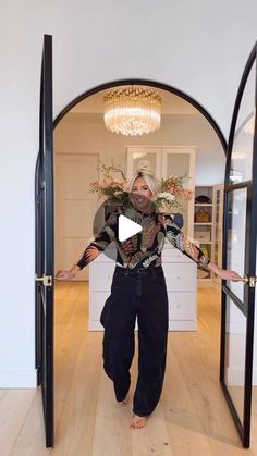 a woman standing in an open doorway with her hands out to the side and holding flowers