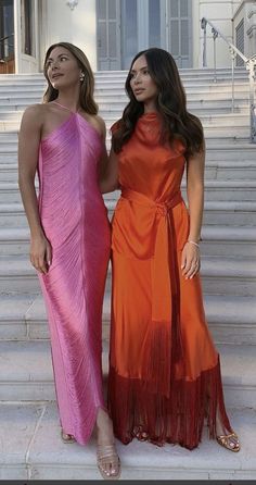 two women standing next to each other in front of stairs wearing dresses with tassels