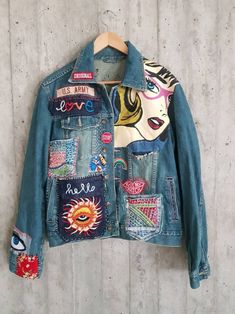 a jean jacket with patches on the back and an eye patch on the front, hanging against a wall